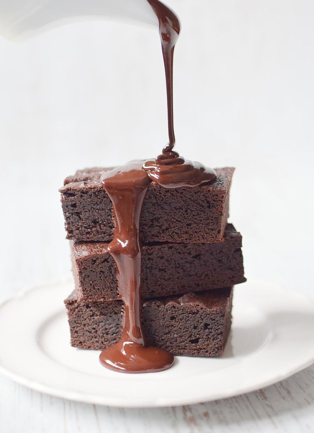 Pouring melted chocolate over a stack of brownies